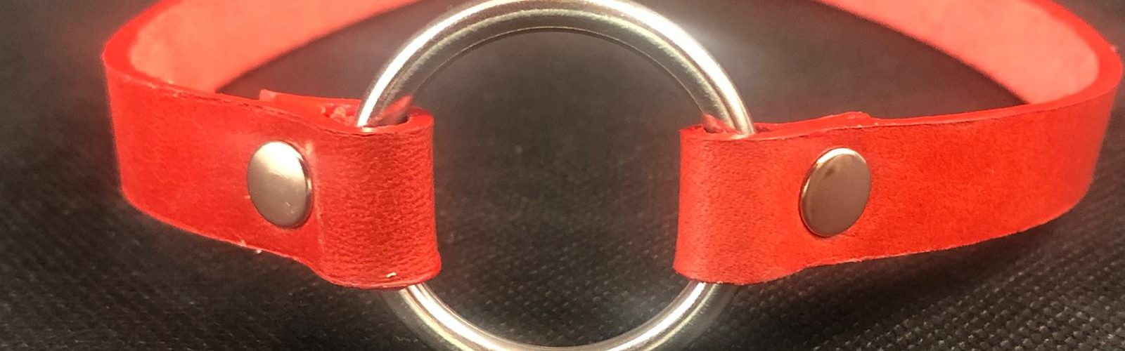 Red leather choker with silver coloured o-ring at the front and simple silver coloured buckle at rear.